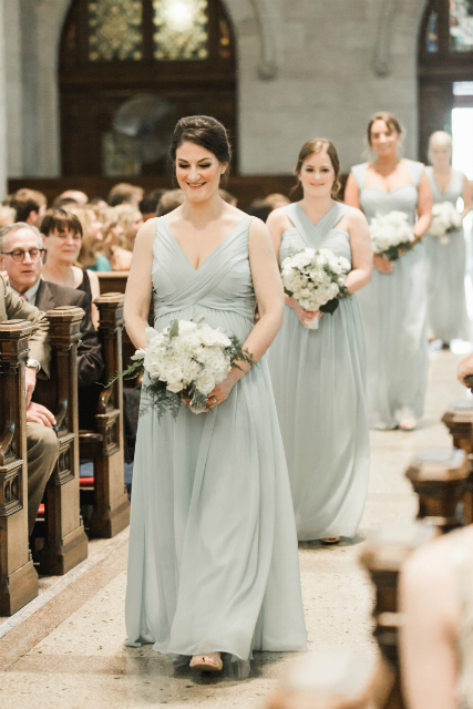 bridesmaids walking down the aisle wearing mint color dresses and holding an all white bouquet