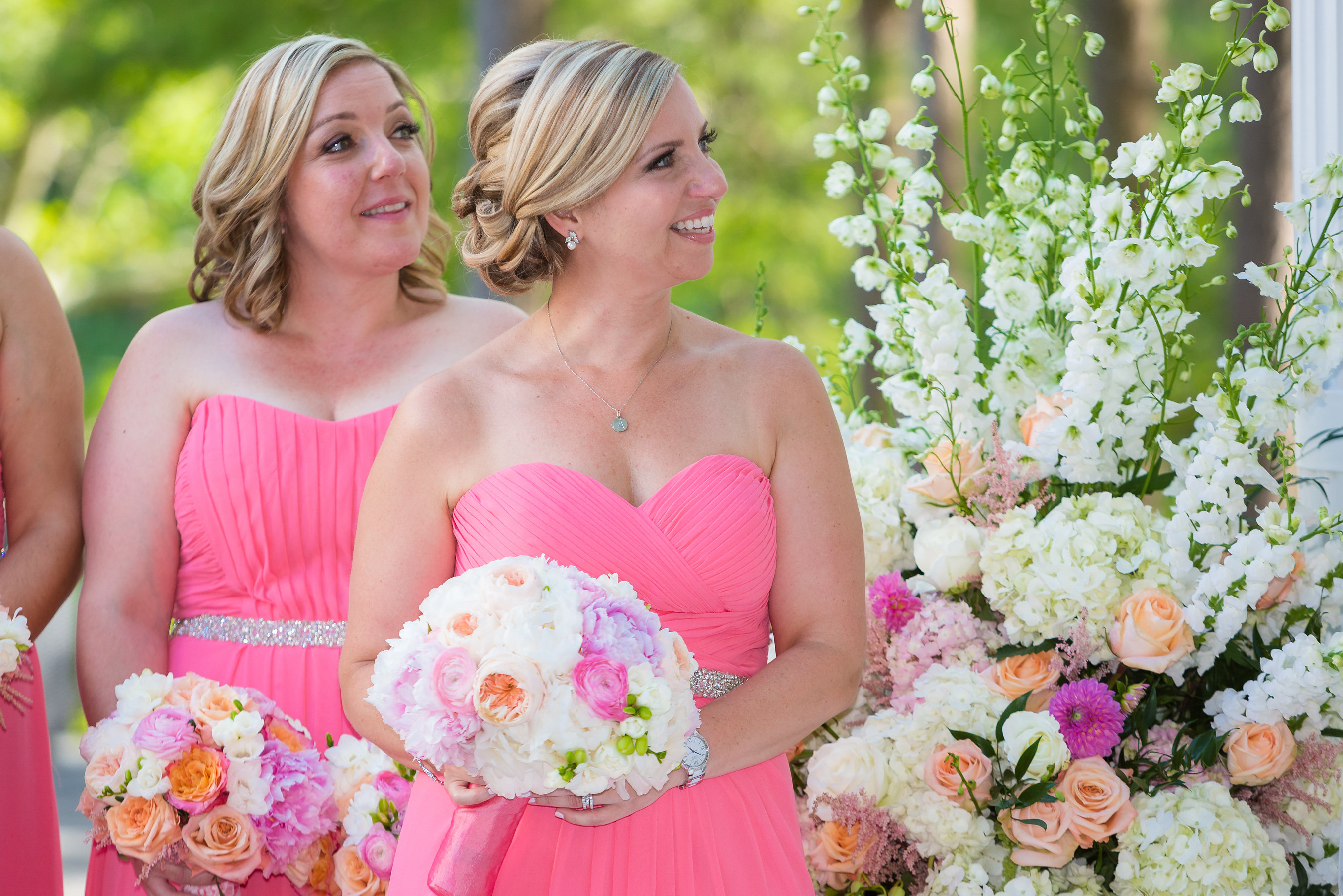 Bridemaids wearing pink dresses surrounded by a floral display at the ceremony