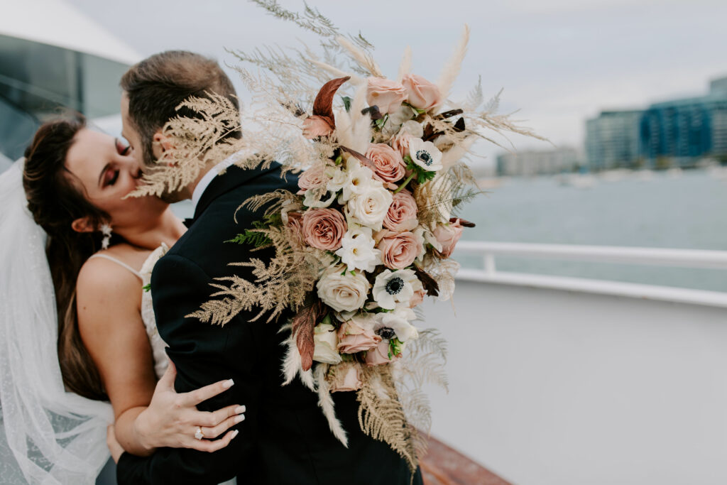Warm tone bridal bouquet highlighted with tinted-gold plumosas, pampas grass plumes, and brown feathers by Stapleton Floral
