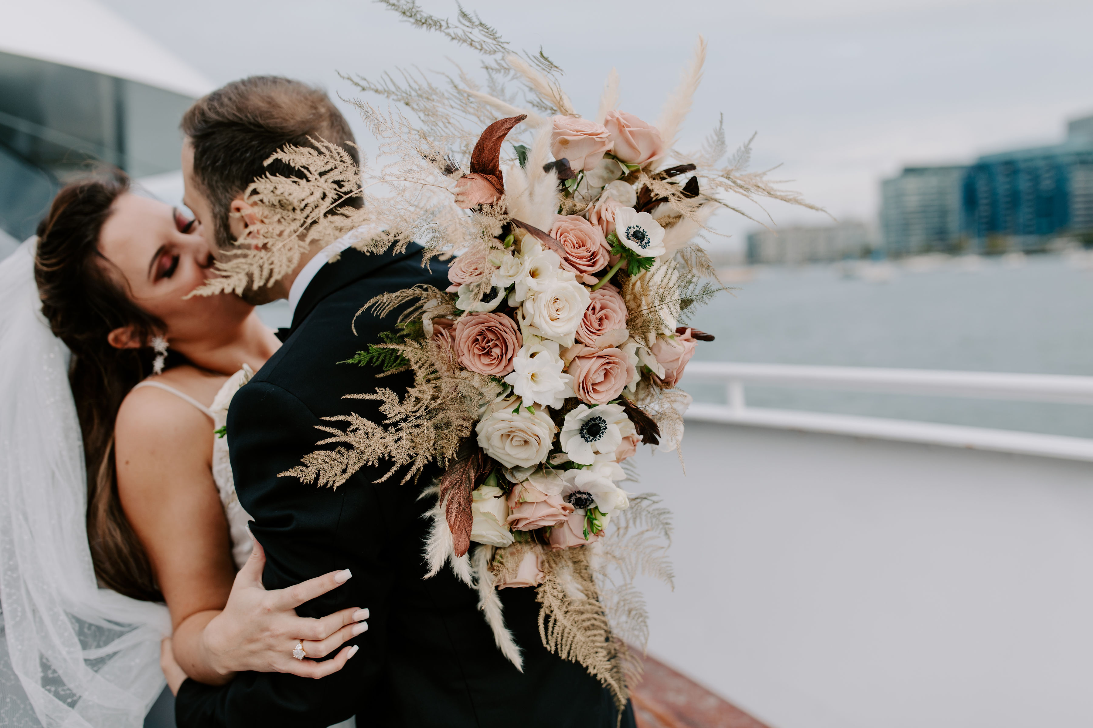 Warm tone bridal bouquet highlighted with tinted-gold plumosas, pampas grass plumes, and brown feathers by Stapleton Floral