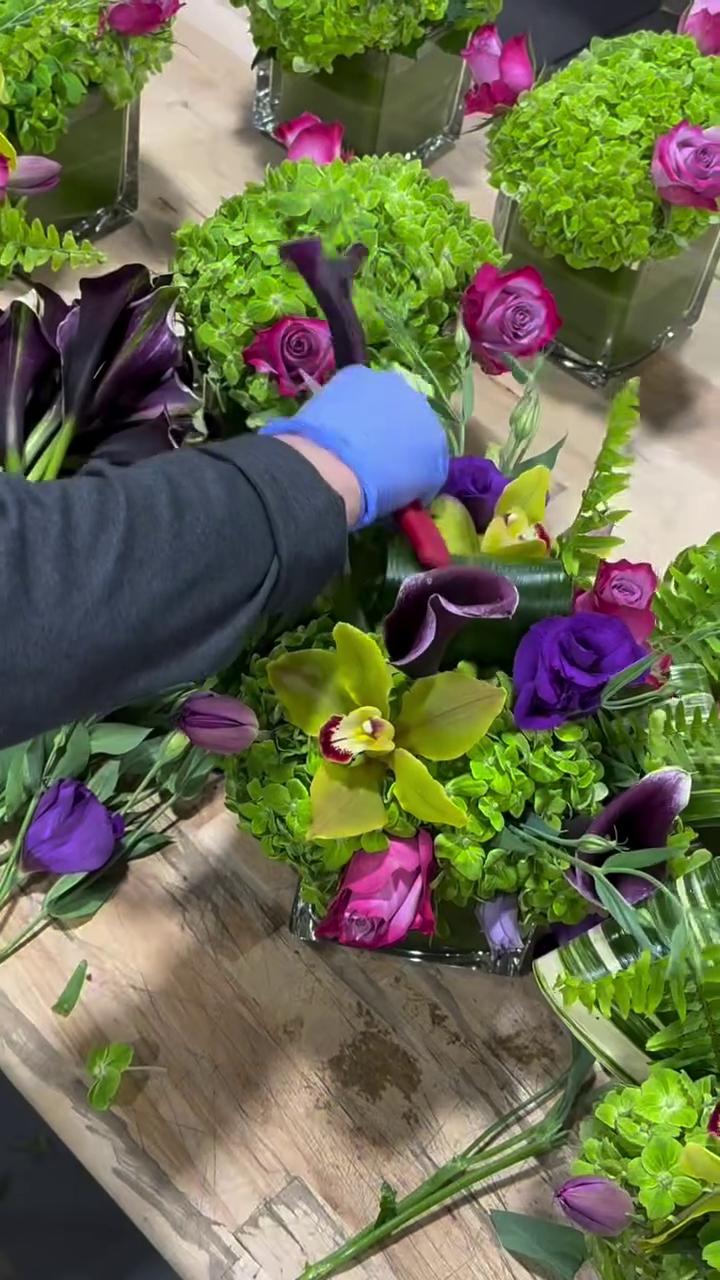 Floral designer arranging jewel-toned and yellow blooms in cube vases for a custom event centerpiece.