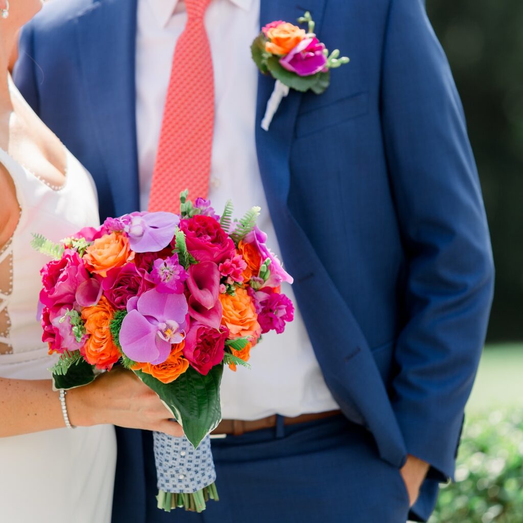 Bride and groom holding a vibrant summer wedding bouquet with orchids, roses, and bold pink and orange florals.