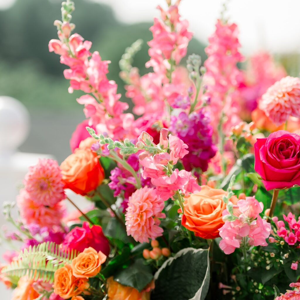 Close-up of summer wedding flowers featuring pink snapdragons, orange roses, and vibrant dahlias in a bright floral arrangement.