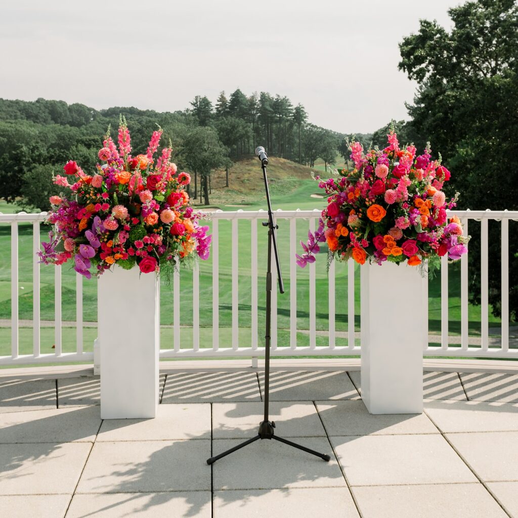 Summer wedding ceremony setup with bright floral arrangements on pedestals overlooking a Boston-area golf course.