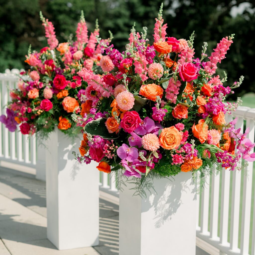 Colorful summer wedding flowers with roses, orchids, and dahlias on tall white pedestals in Boston.