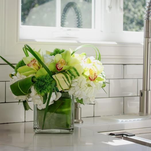 Classic Monochrome floral arrangement in a glass vase, featuring green orchids, white hydrangeas, and tropical greenery, displayed on a bright kitchen countertop in South Boston.