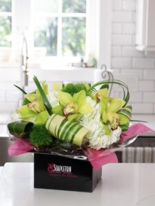 Bright green orchid floral arrangement with white hydrangeas in a black Stapleton Floral box on a kitchen counter