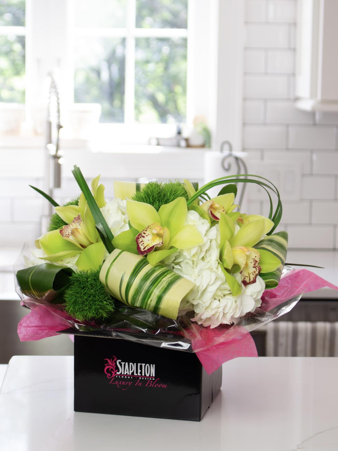 Bright green orchid floral arrangement with white hydrangeas in a black Stapleton Floral box on a kitchen counter