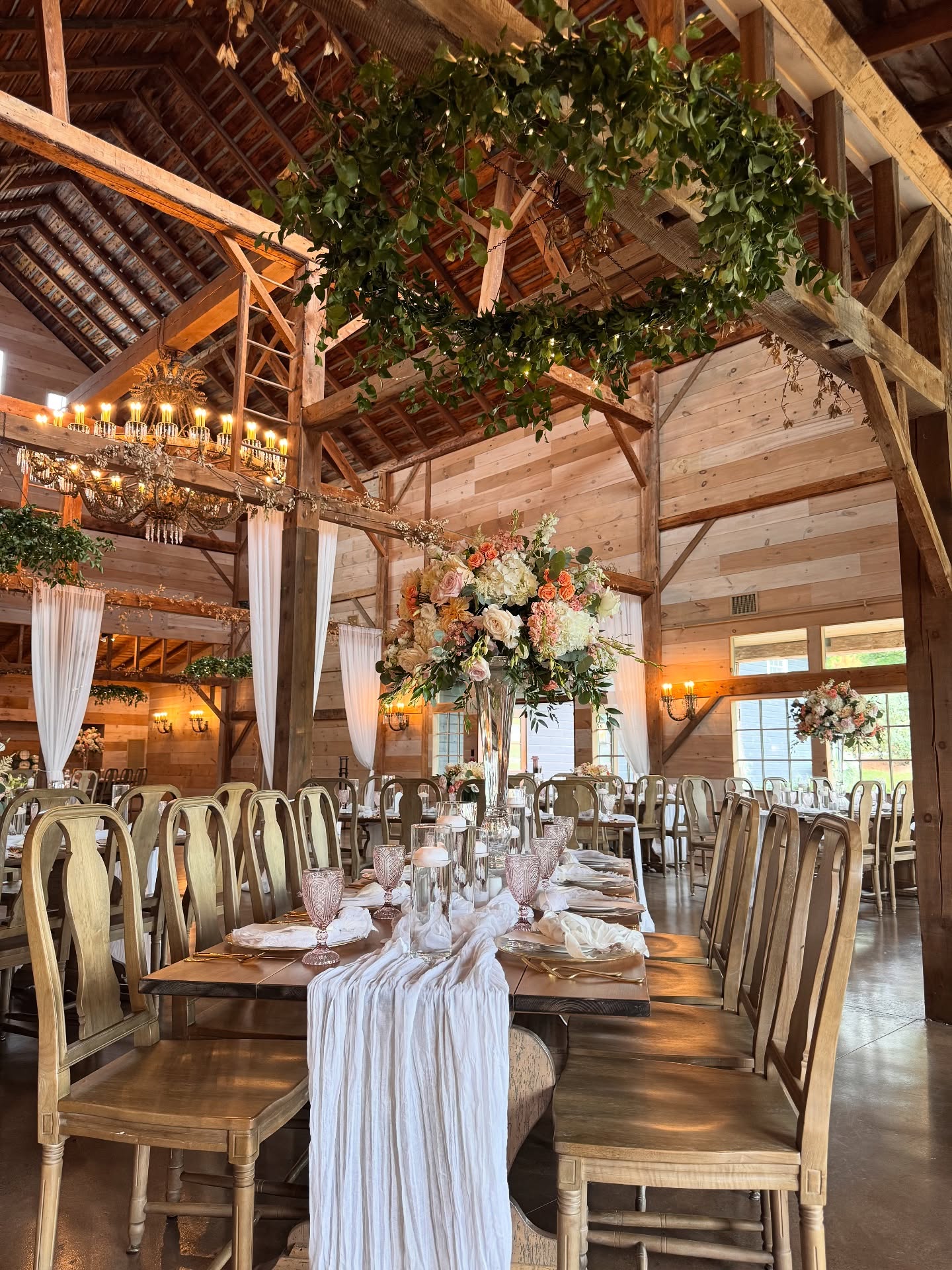 Elegant wedding reception table at The Sablewood with tall floral centerpiece, draped runner, and rustic wooden chairs