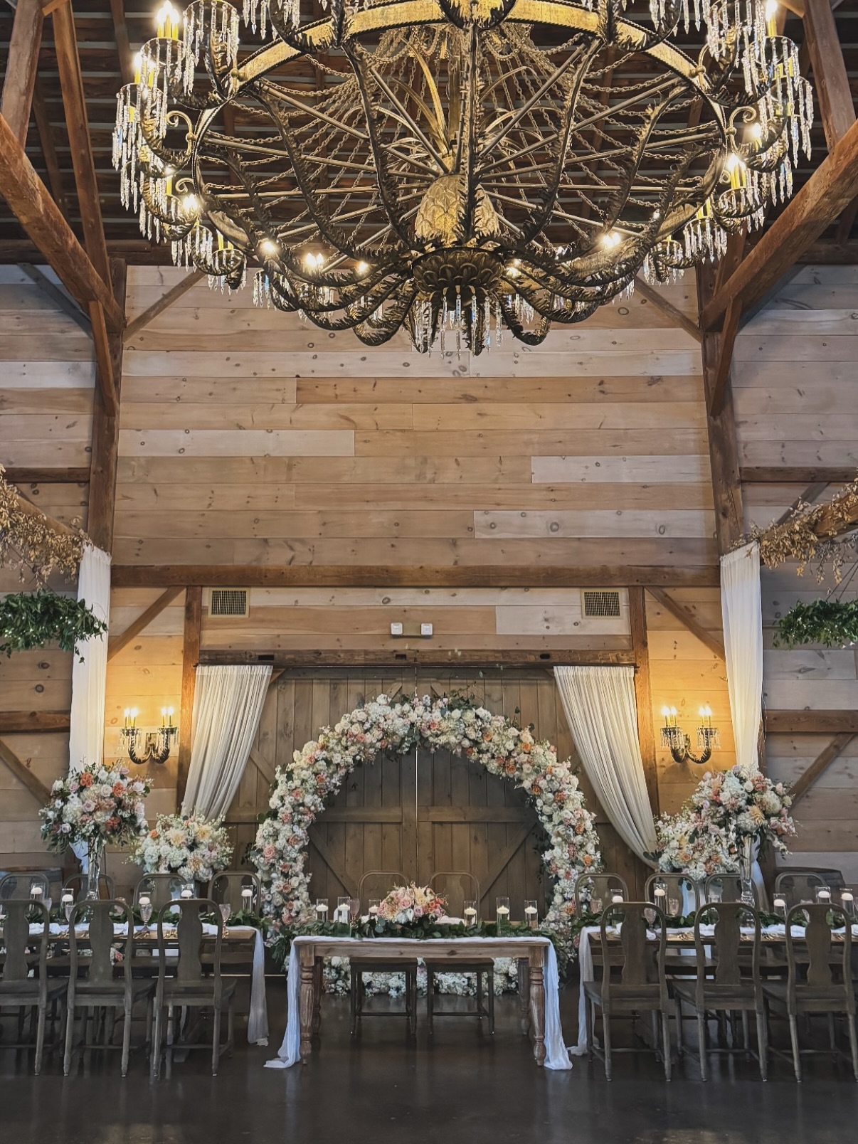 Grand floral arch and chandelier inside The Sablewood wedding venue with lush flowers and rustic wooden details
