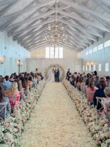 Bride and groom at the altar with a rose petal aisle lined by floral arrangements during a wedding ceremony at The Sablewood