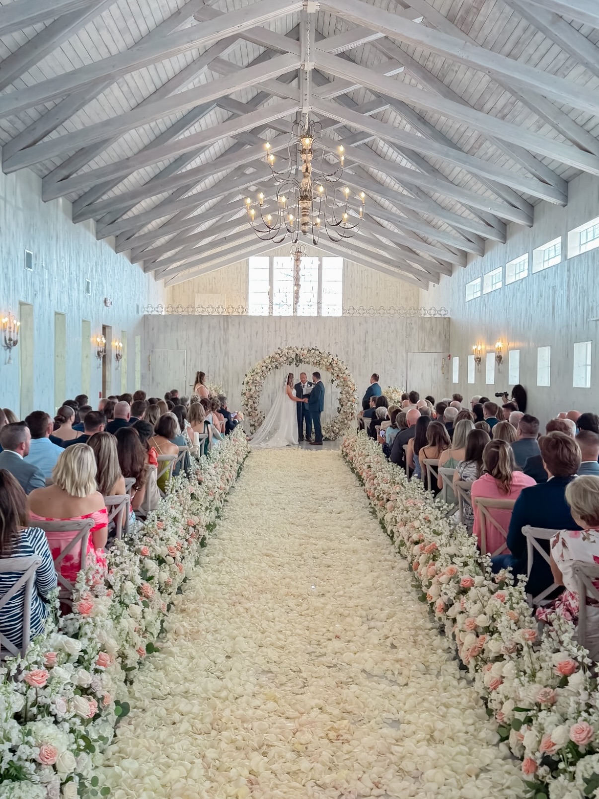 Bride and groom at the altar with a rose petal aisle lined by floral arrangements during a wedding ceremony at The Sablewood