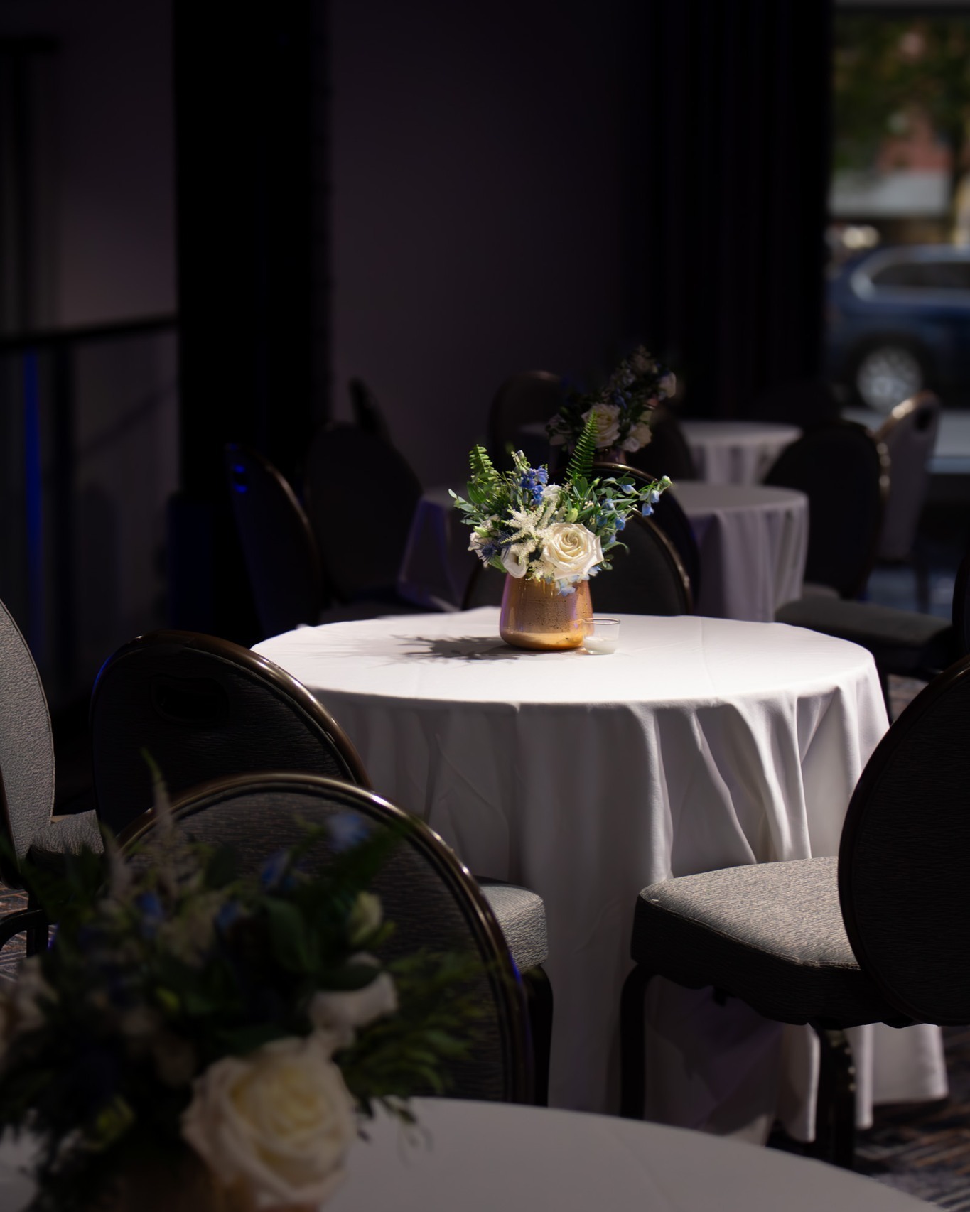 Small gold vase with white and blue floral arrangement on a cocktail table at an elegant reception.