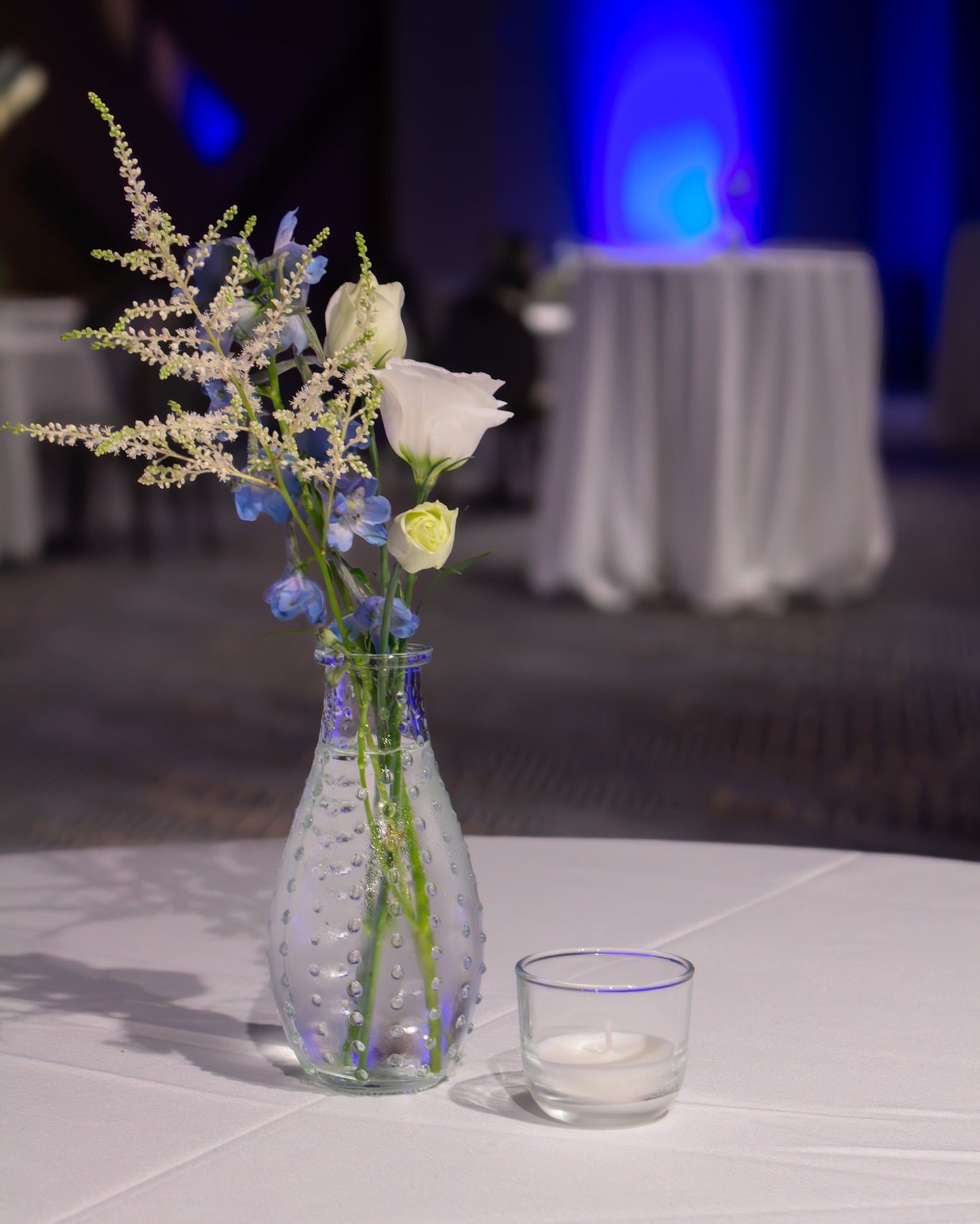Minimal blue and white flowers arranged in a textured glass vase with a candle on a cocktail table.