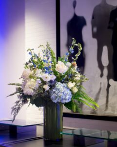 Tall arrangement of blue hydrangeas, white roses, and greenery creating a sophisticated event centerpiece.