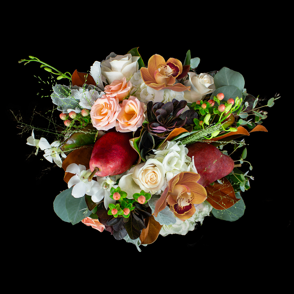 Top view of the Harvest Hearth Thanksgiving floral centerpiece featuring roses, orchids, pears, hydrangea, and autumn greenery on a black background.
