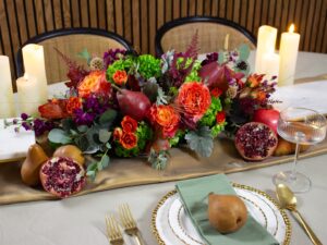 Thanksgiving floral centerpiece with rich autumn blooms, pears, and pomegranates surrounded by candles on an elegant holiday table.