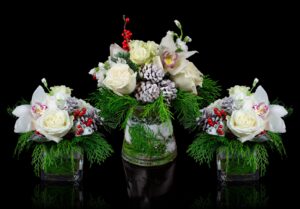 Elegant holiday floral arrangements featuring white roses, orchids, red berries, and frosted pinecones with lush winter greenery, styled for seasonal events and celebrations.