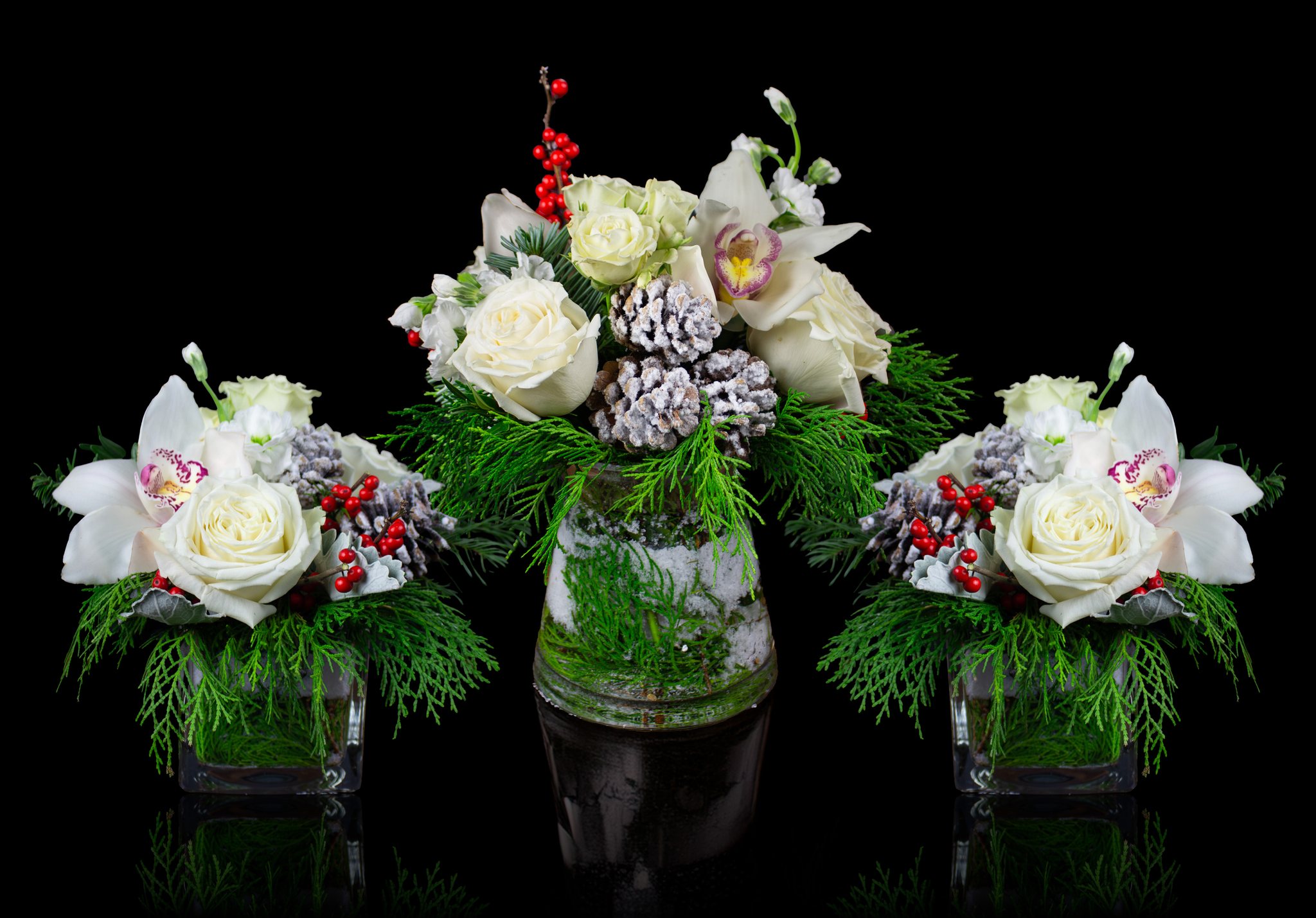 Elegant holiday floral arrangements featuring white roses, orchids, red berries, and frosted pinecones with lush winter greenery, styled for seasonal events and celebrations.
